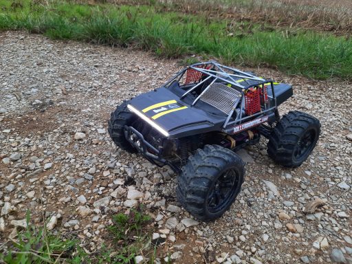 Schwarzes RC-Auto mit großen Reifen auf einem Kiesweg.