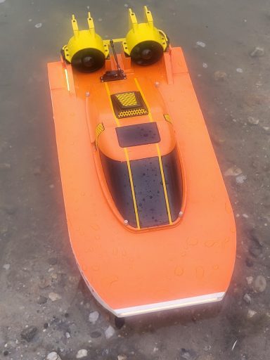 Ein orangefarbenes ferngesteuertes Boot mit gelben Motoren auf dem Wasser.
