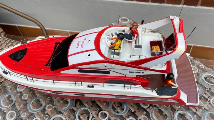 Rotes Modellboot mit Zubehör auf einem gemusterten Untergrund.